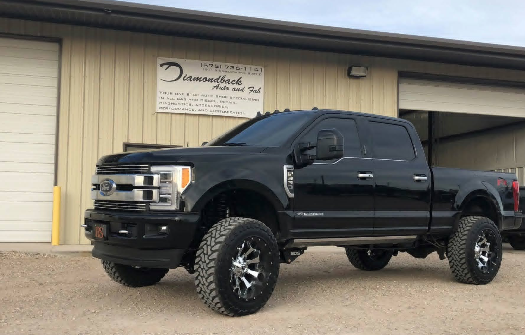 Black lifted Ford truck in front of the shop sign
